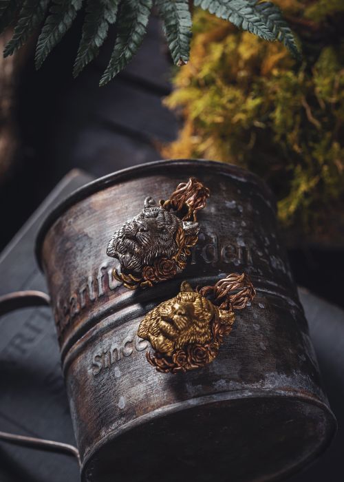 Free Gold and silver tiger-themed brooches on a vintage iron cup, surrounded by ferns. Stock Photo