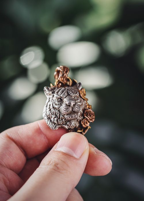 Free Closeup of a hand holding a detailed silver and bronze brooch featuring a lion and floral design. Stock Photo
