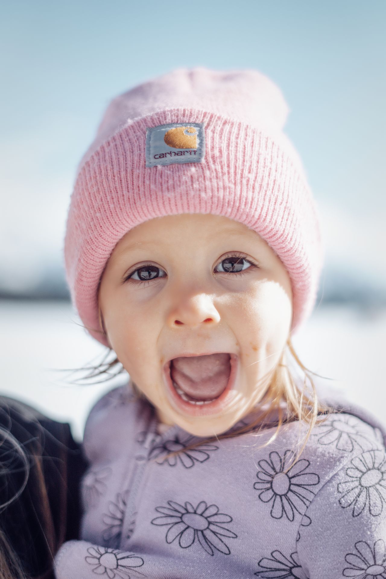 Laughing toddler wearing a pink knit winter beanie in the snow