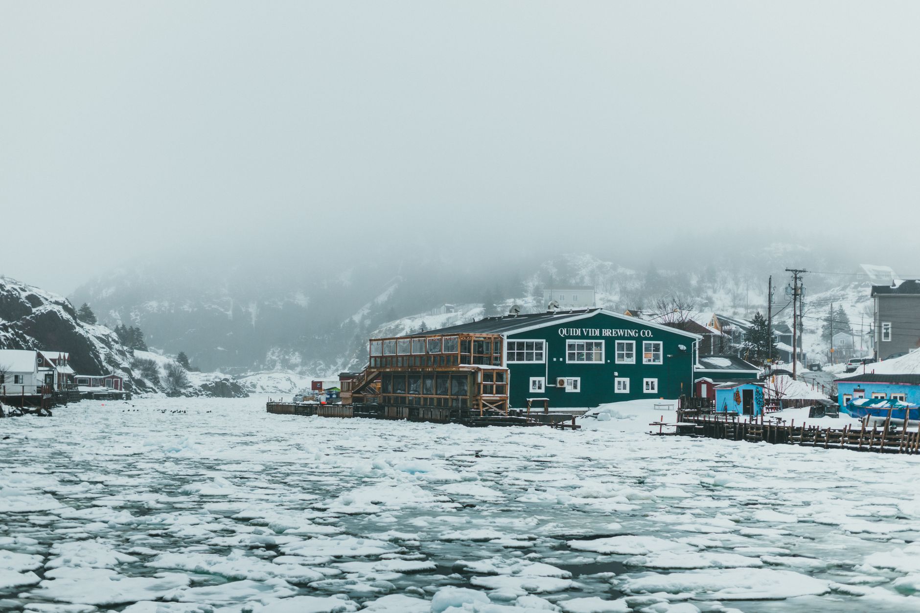 A wintry scene of Quidi Vidi Village with ice-covered waters and misty hills in Newfoundland.