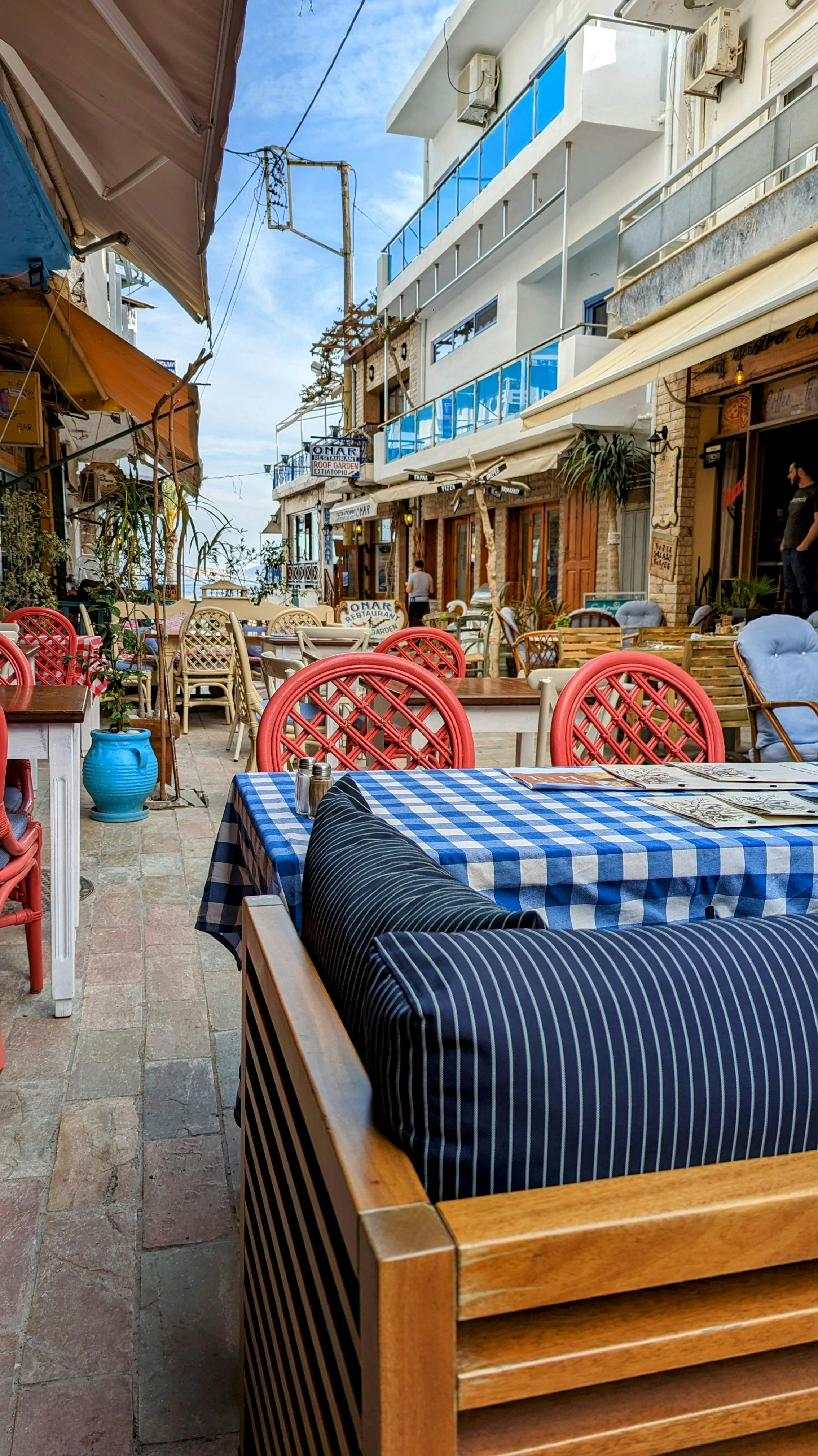 Terrasse de café grec avec nappes à carreaux bleus et blancs dans une ruelle