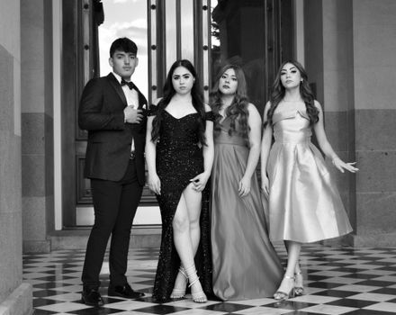 A group of elegantly dressed young adults posing in formalwear outside a grand entrance.