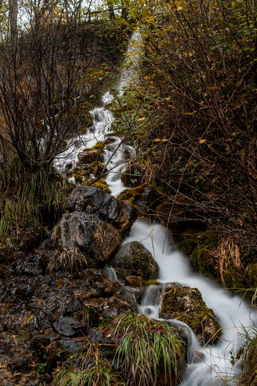 Free A picturesque cascade of water flows through rocks and foliage in an autumn forest landscape. Stock Photo