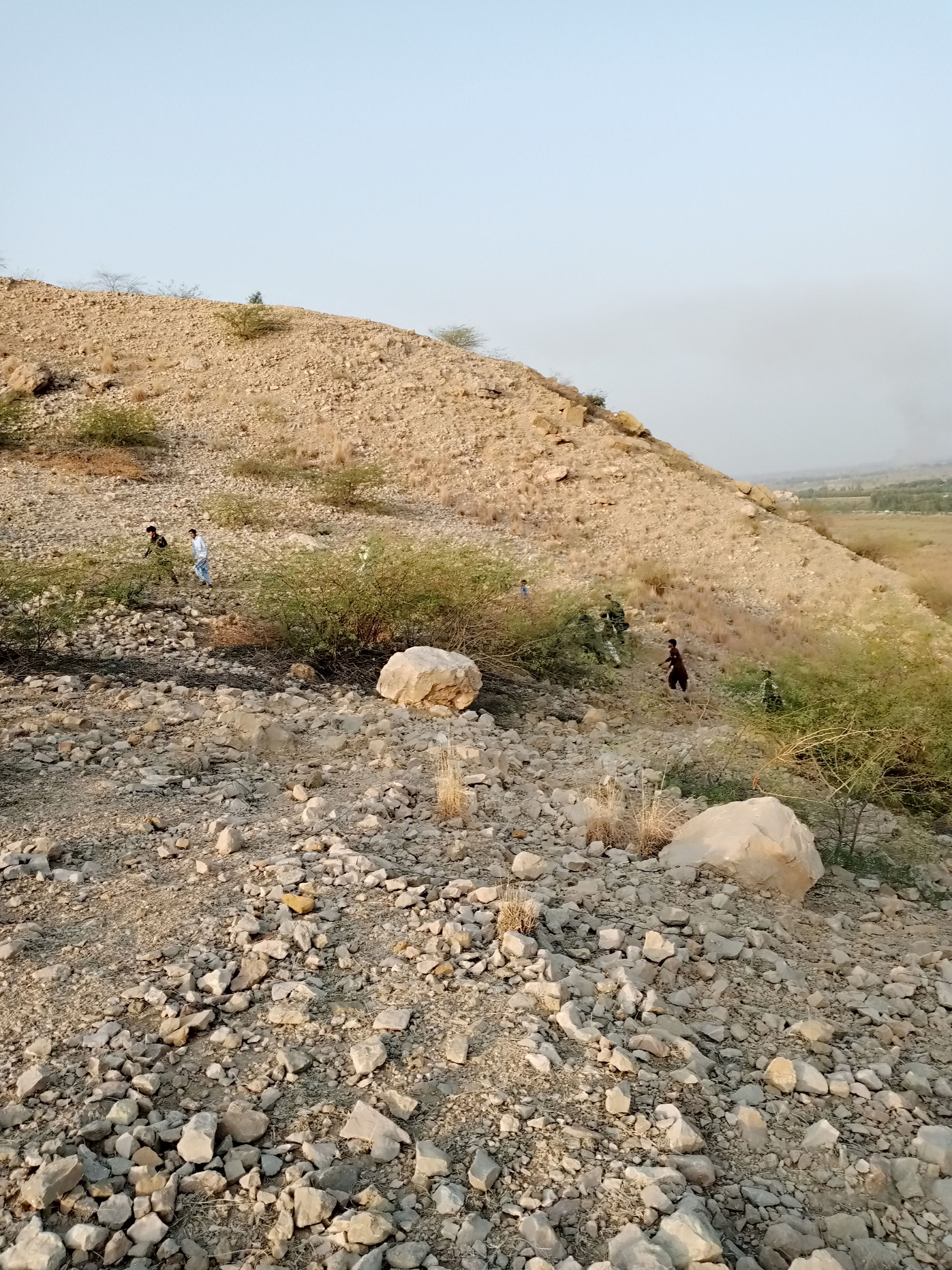 A group explores the rocky landscape of Dera Ismail Khan under a clear blue sky.