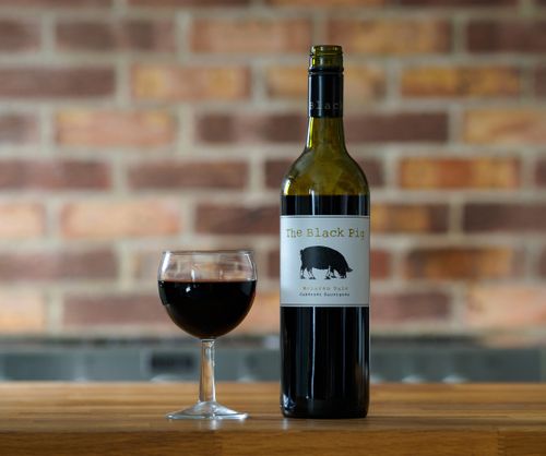 Free Bottle of The Black Pig wine with a glass, set against a brick wall backdrop. Stock Photo