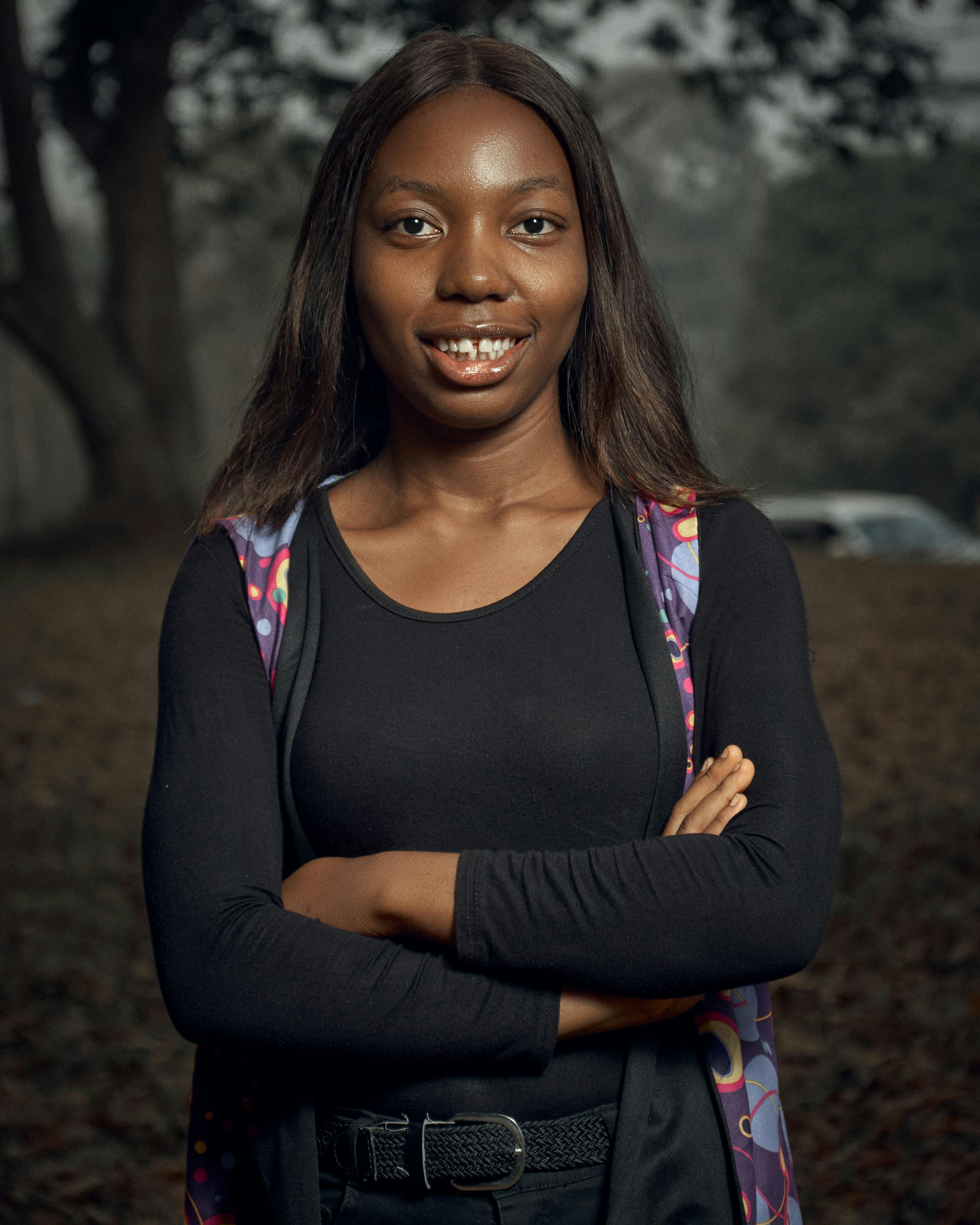 A smiling woman posing confidently outdoors in Ife, Nigeria, wearing a black top and colorful scarf.