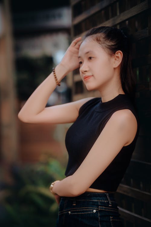 Young Woman in a Black Top and Jeans Standing against a Wall Outside 