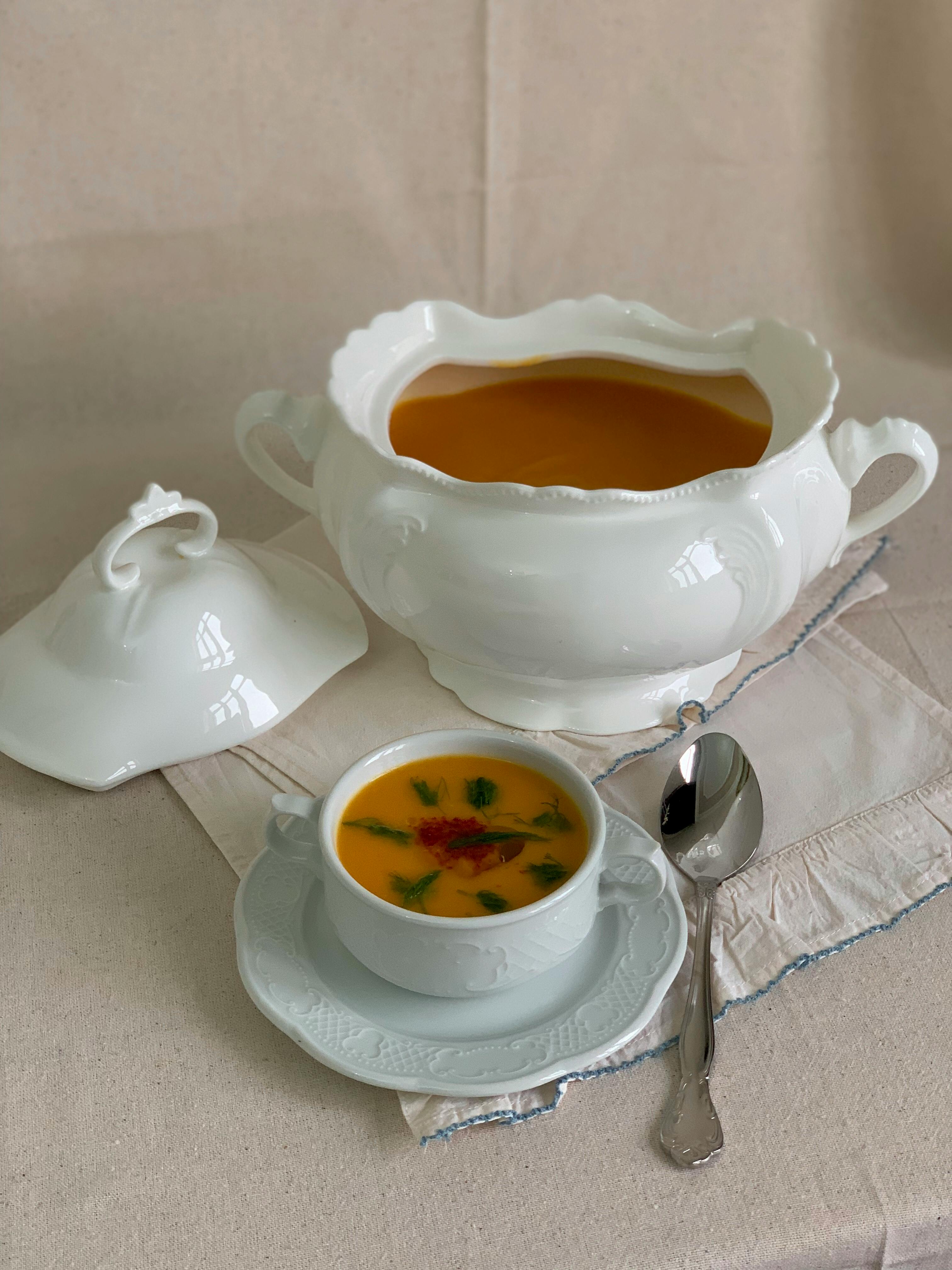 High-angle view of carrot soup elegantly served in white porcelain with a matching tureen and spoon.