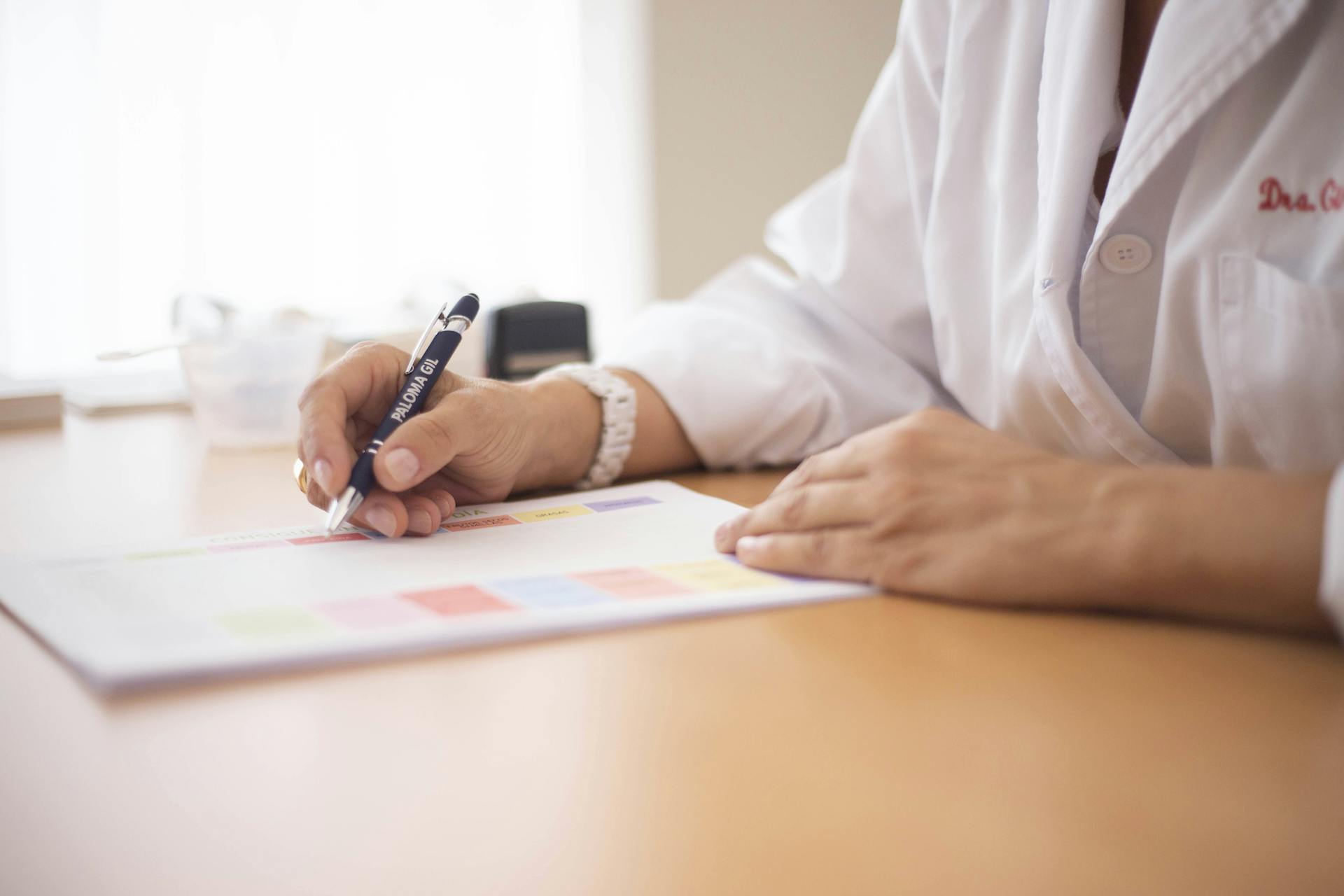 Close-up of a female doctor writing a prescription at a desk in an office setting.