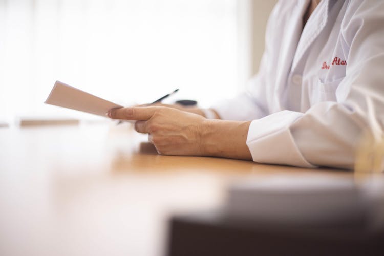 Close-up Of A Doctor Sitting At A Desk And Holding A Document 