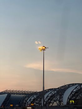 View of a modern airport structure at dusk with a glowing lamp post against the sky.