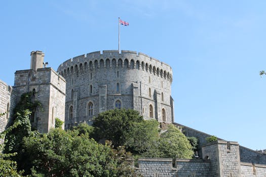 Stone tower of Windsor Castle with Union Jack against a clear blue sky. by Kris Schulze