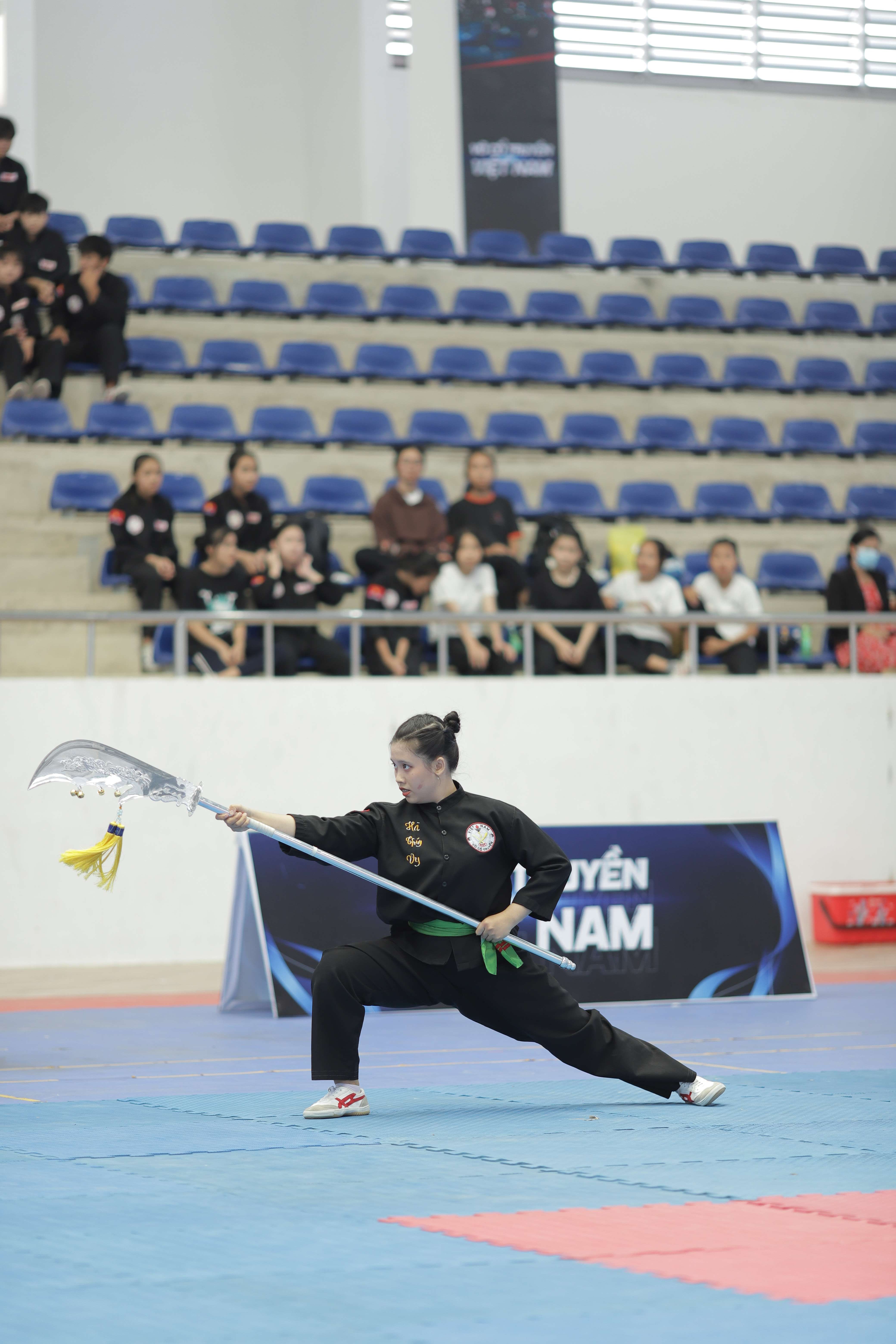 Woman practicing martial arts with a traditional weapon in an indoor sports hall.