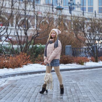 Woman dressed in winter fashion posing on a snowy urban street, showcasing style and elegance.