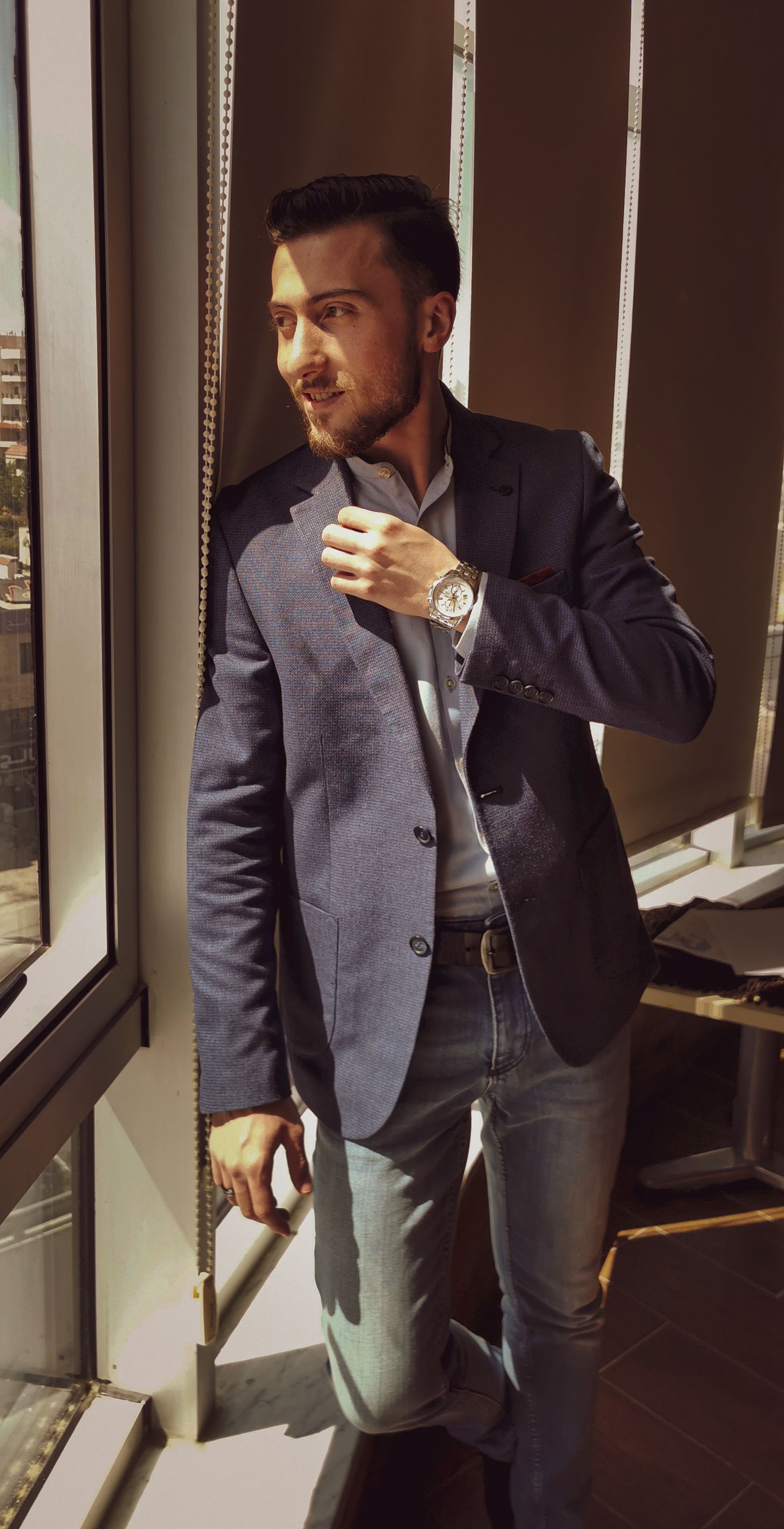 Fashionable man in casual business attire standing by window in Amman, Jordan.