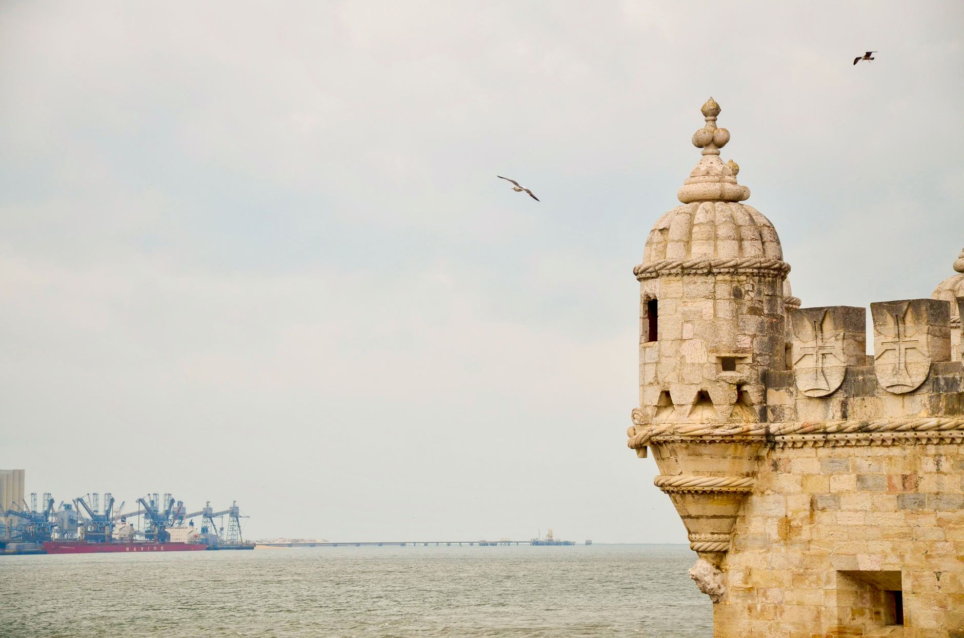 Scenic view of Belem Tower by the Tagus River in Lisbon, Portugal with birds in flight.