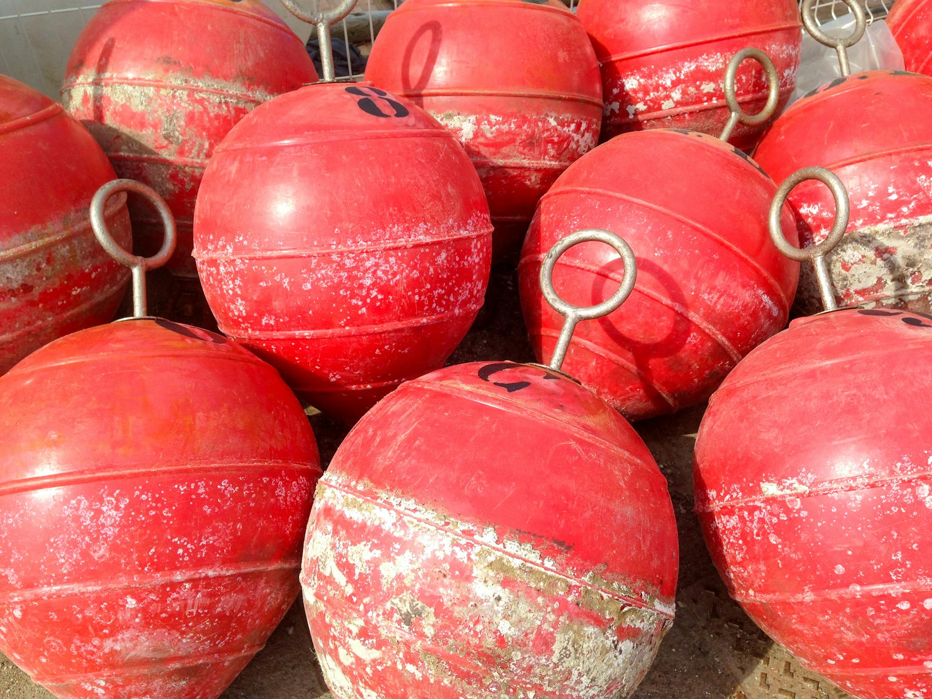 Red marine buoys with metal handles on an IB dock in Spain, showing signs of wear.