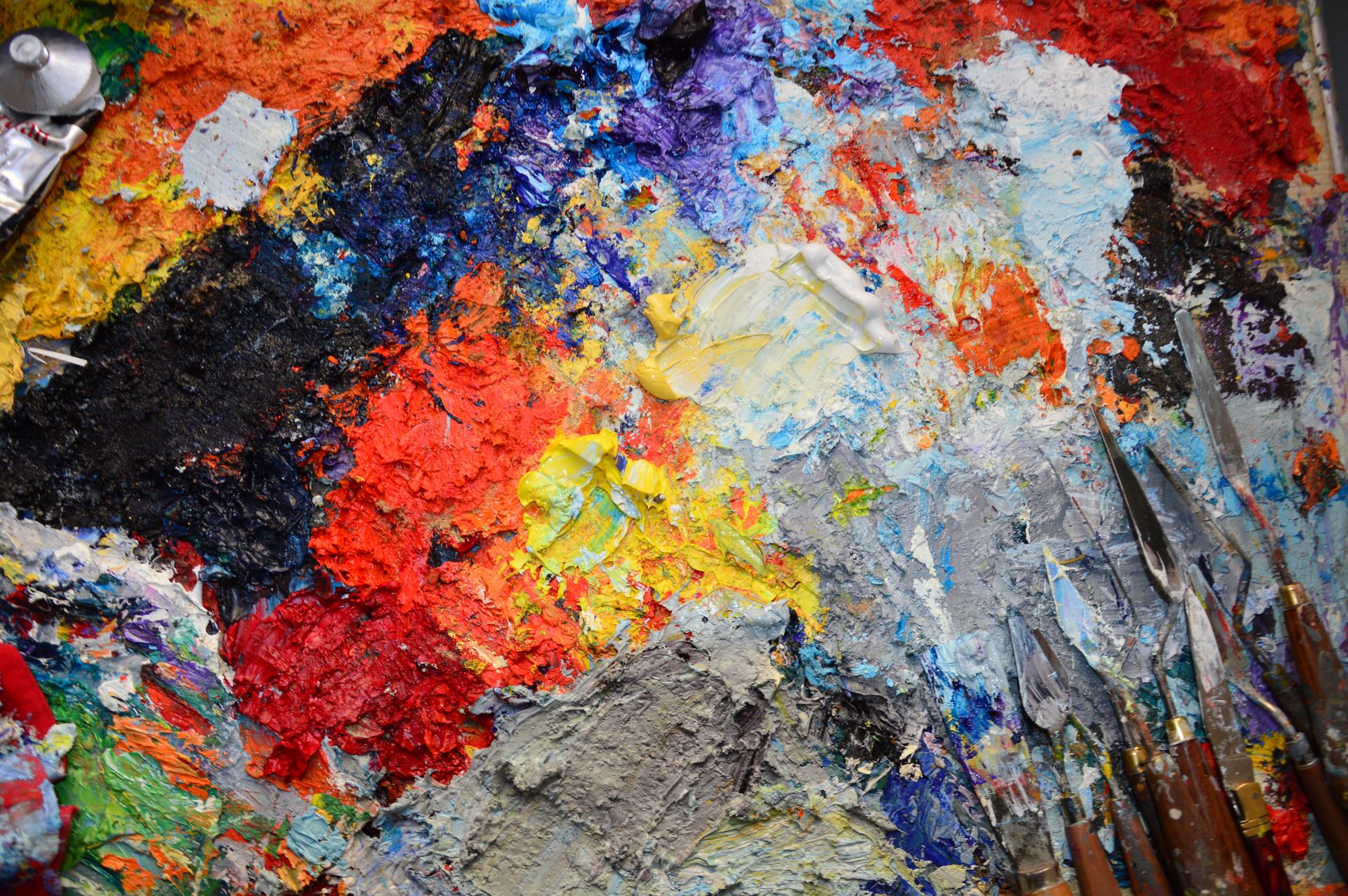 Close-up of a vividly colorful artist's palette with a mix of paints and spatulas.