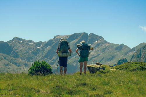 Free Two hikers with backpacks enjoying a mountain view under a clear sky. Stock Photo