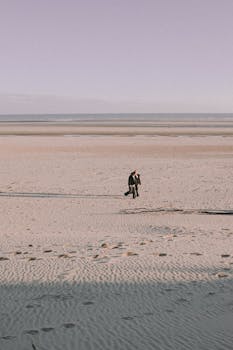 Single person walking on a vast, calm beach during twilight. Tranquil and contemplative scene.
