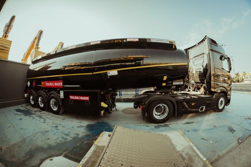 Free Side view of a black tanker truck parked at an industrial shipping facility under clear skies. Stock Photo