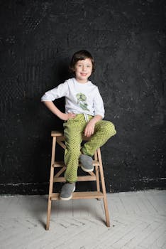 一个穿着绿色裤子的小孩在木梯上摆出时尚姿势，非常适合生活方式和时尚主题