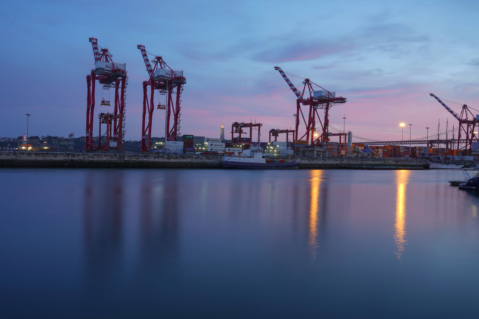 Container cranes on a harbour quay at dusk, reflected in still water