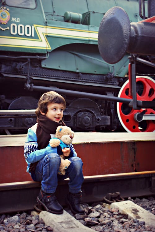 бесплатная Мальчик сидит возле поезда, держа в руках плюшевую игрушку Стоковое фото