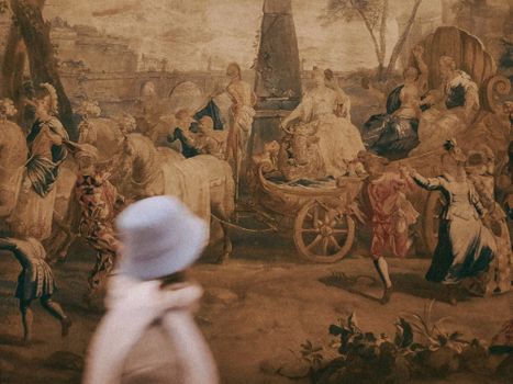 Blurred figure walking past a historical tapestry in Italy, capturing motion and art.