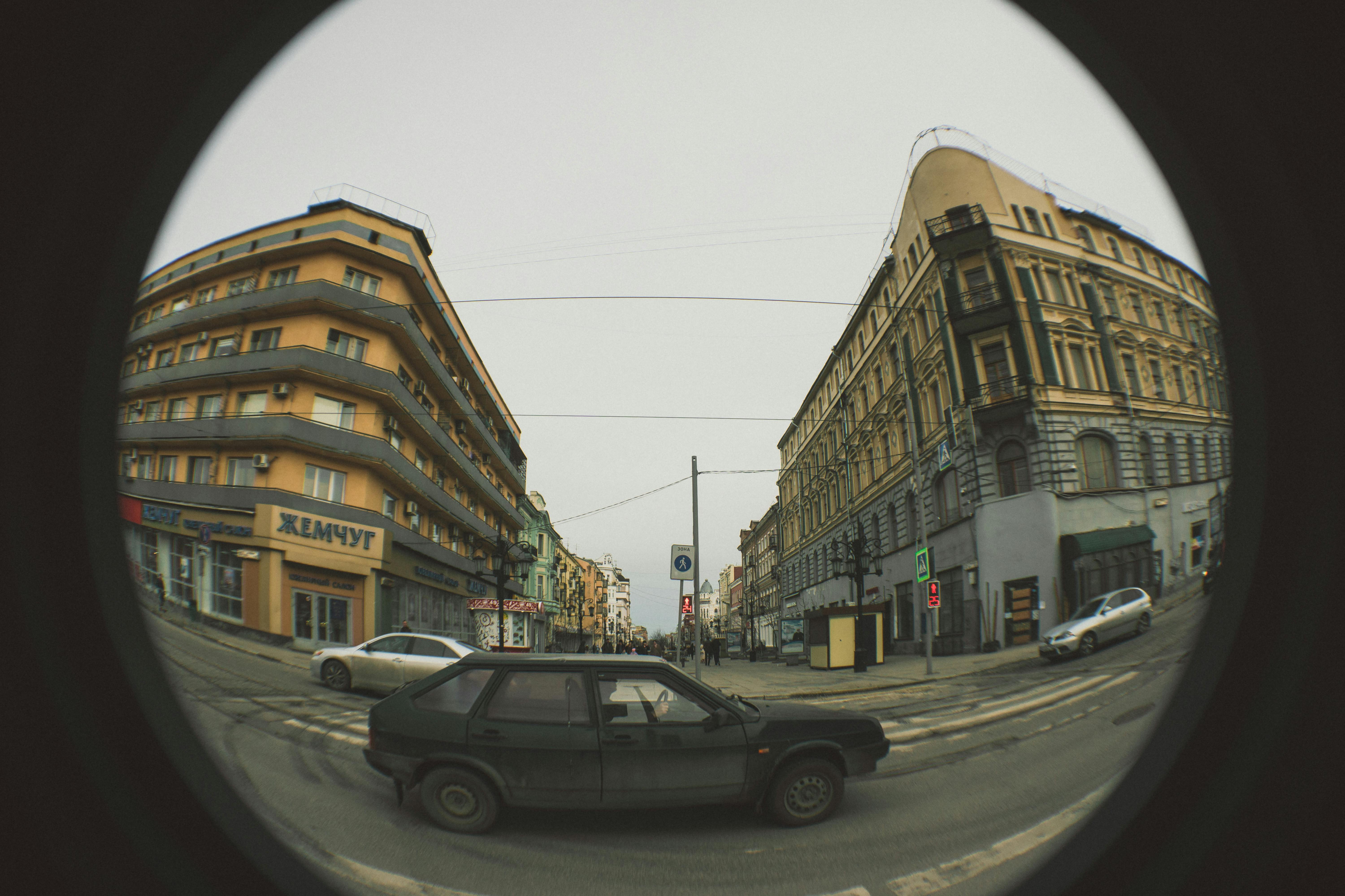 Fisheye lens captures a dynamic city street corner with vintage buildings and passing vehicles.