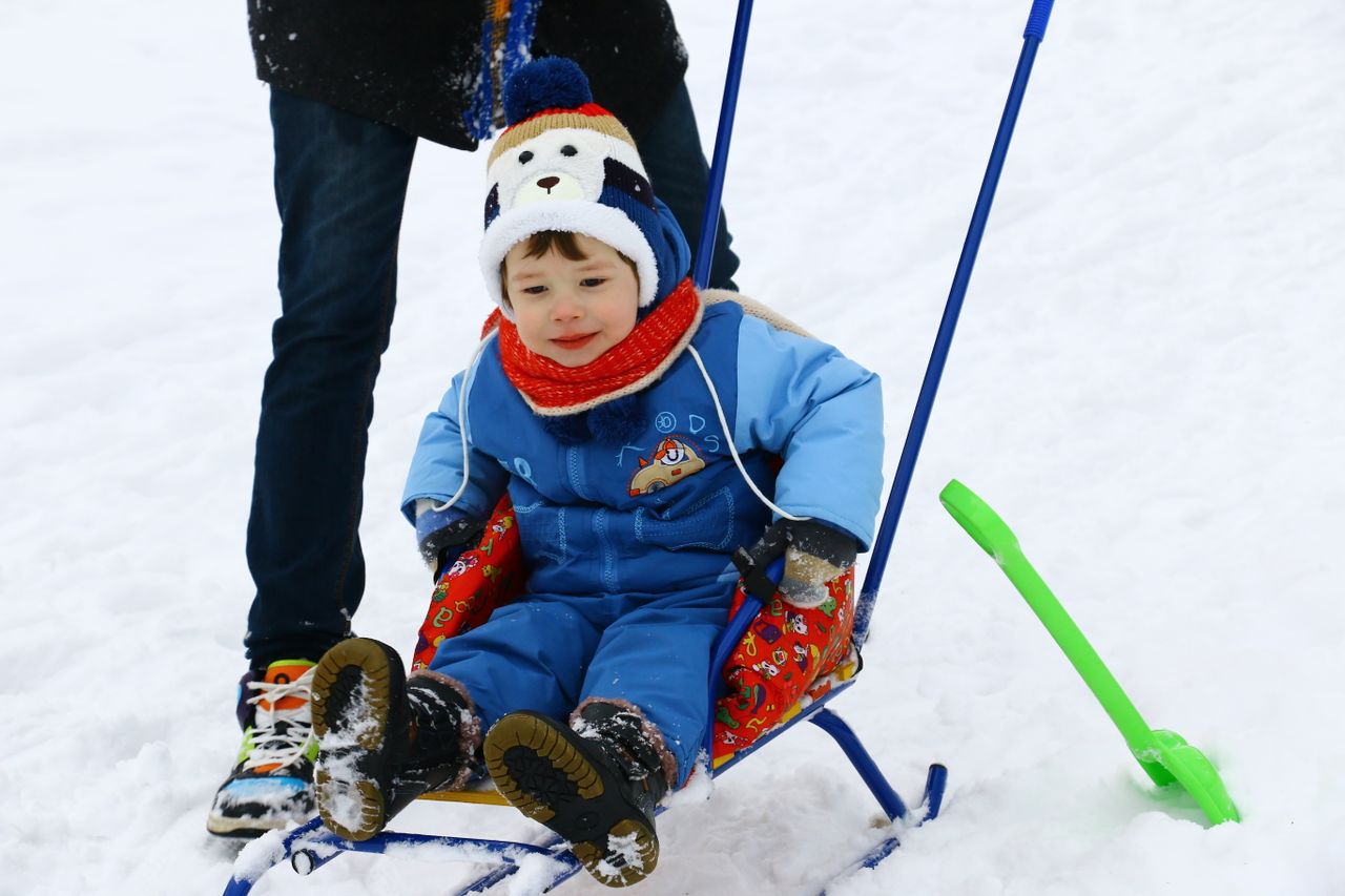 Toddler wearing winter boots riding a sled through snow