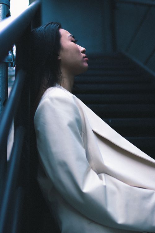 Free Side view of a thoughtful woman in a white blazer resting on stairs. Stock Photo