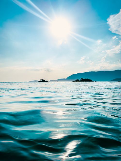 Free A tranquil ocean view under bright sun with clear skies and distant islands. Stock Photo