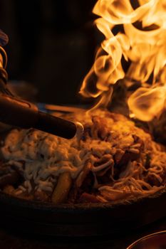 Close-up of a dish with noodles and vegetables being flambéed, highlighting food preparation.
