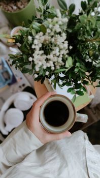 A hand holding coffee near white flowers, capturing a cozy morning vibe.