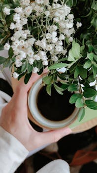 A serene moment captured with a hand holding coffee surrounded by white blooms in Göynük, Türkiye.