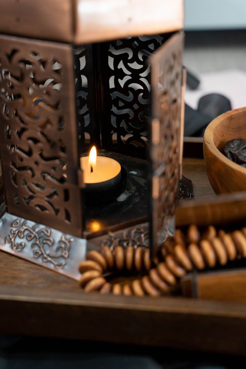 Free Elegant bronze lantern with a lit candle, surrounded by wooden beads and a bowl, creates a serene atmosphere. Stock Photo