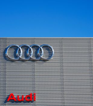 Close-up of an Audi building showcasing its logo against a bright blue sky. 16212217