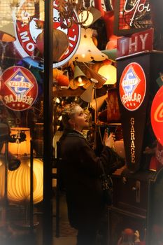 A young woman admires vintage signs and lamps in an eclectic, neon-filled antique store.