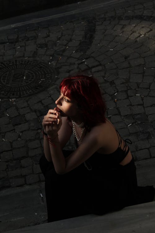 Young Redhead Sitting on a Cobblestone Street at Night