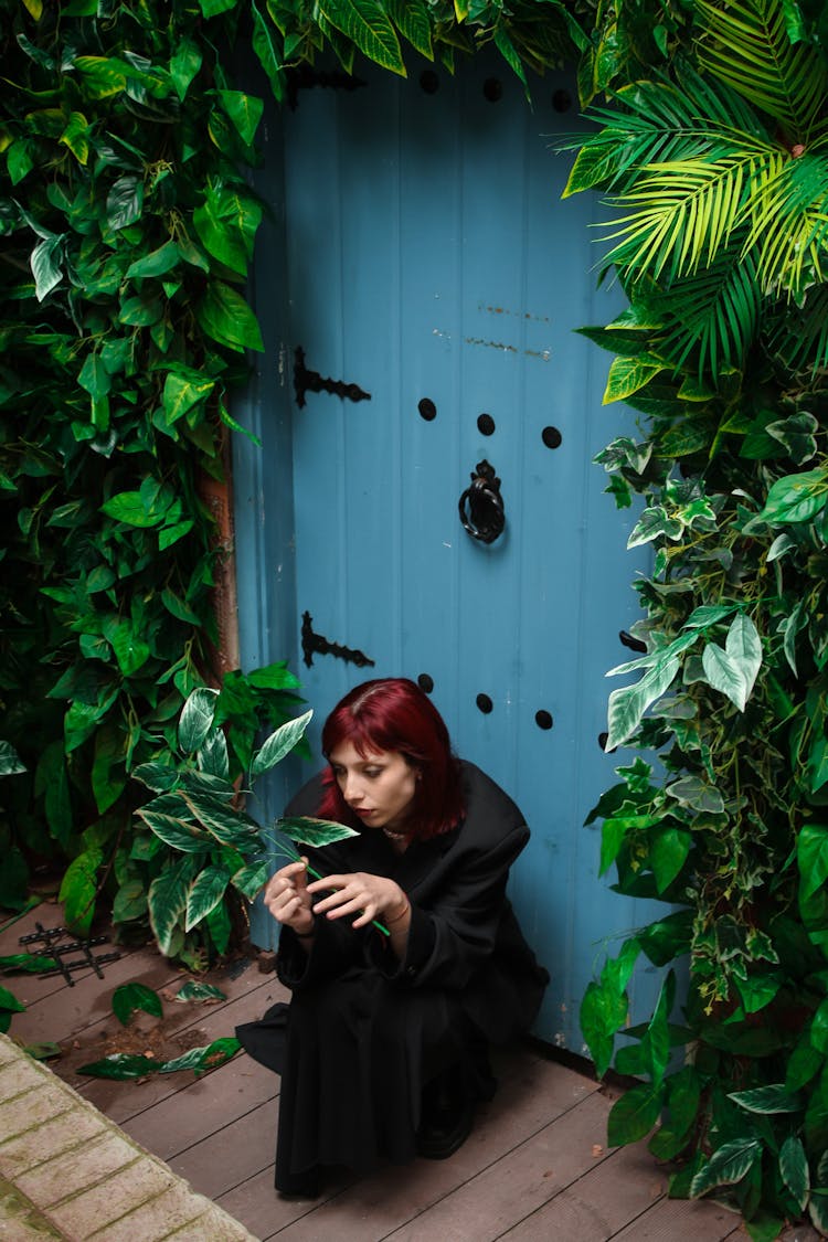 Young Woman Crouching In Front Of An Overgrown Door