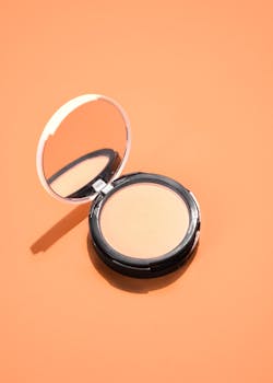 High angle view of a compact powder with mirror on a vibrant orange surface.