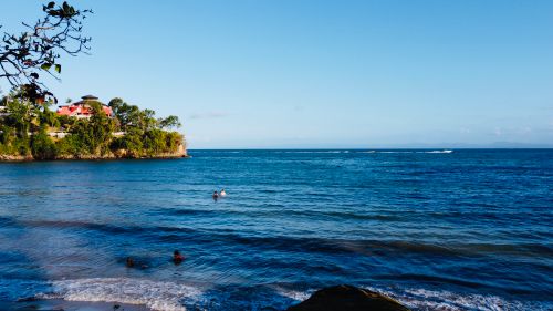 Free Beautiful red-roofed houses on a lush peninsula, swimmers in ocean, clear summer day. Stock Photo
