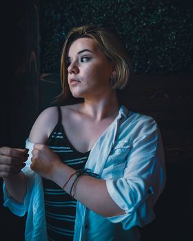A young woman in a striped top poses thoughtfully indoors, casting a sideward glance. The image conveys a moody yet casual atmosphere.