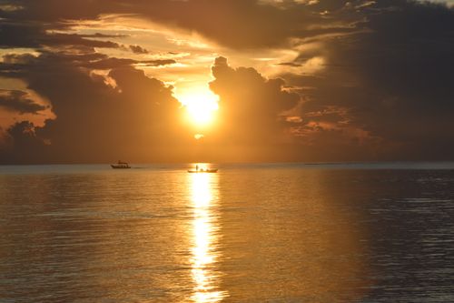 Free Captivating sunset over a serene ocean with silhouetted boats, perfect for travel and tourism themes. Stock Photo