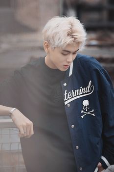 Fashionable young man with blonde hair wearing a navy jacket and t-shirt, posing outdoors.