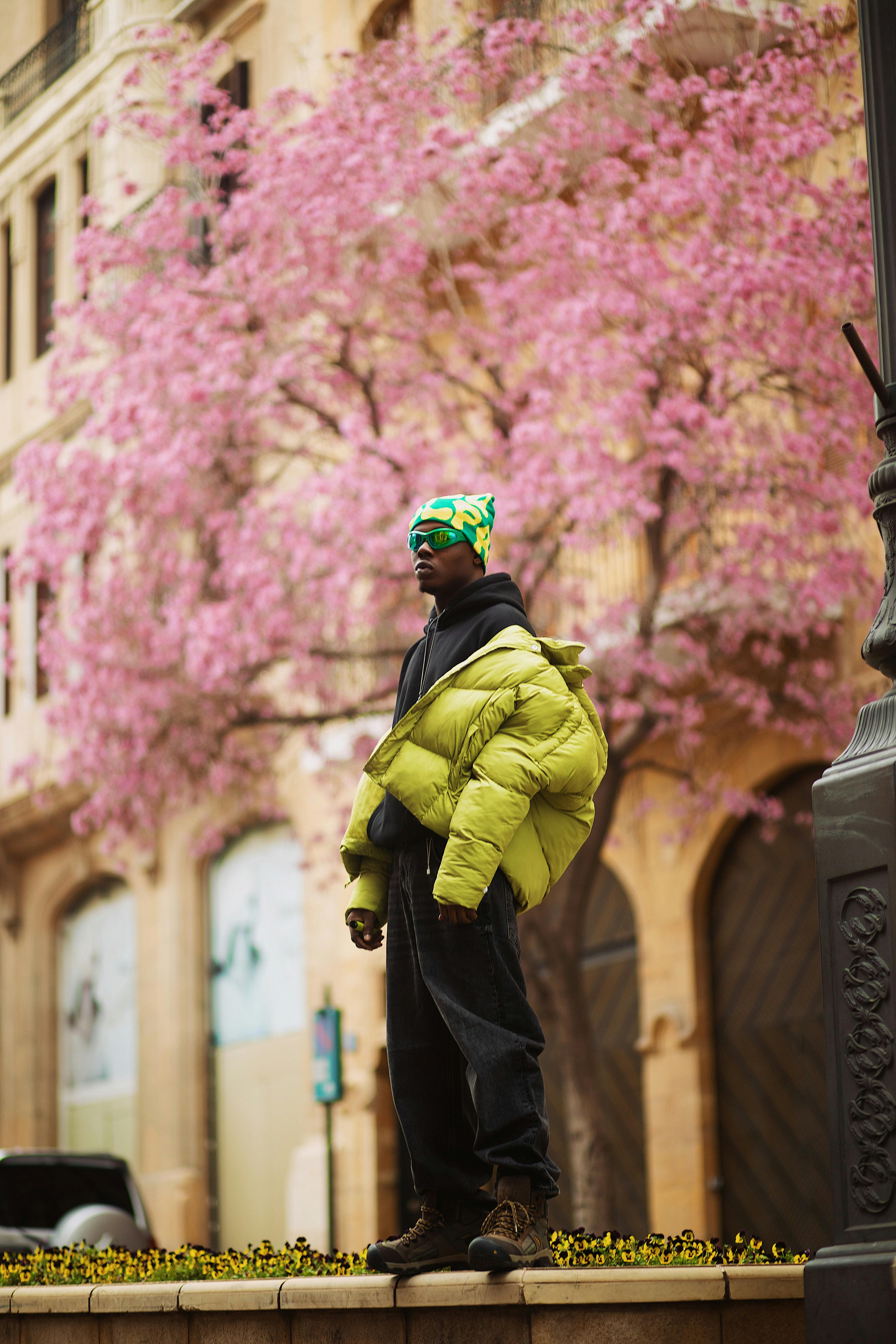 Fashionable model in vibrant puffer jacket posing with Beirut's city charm and blooming pink trees.