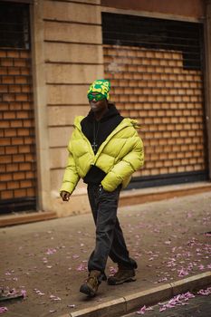 Fashionable individual in bright attire walks along a flower-strewn sidewalk in Beirut's urban landscape.