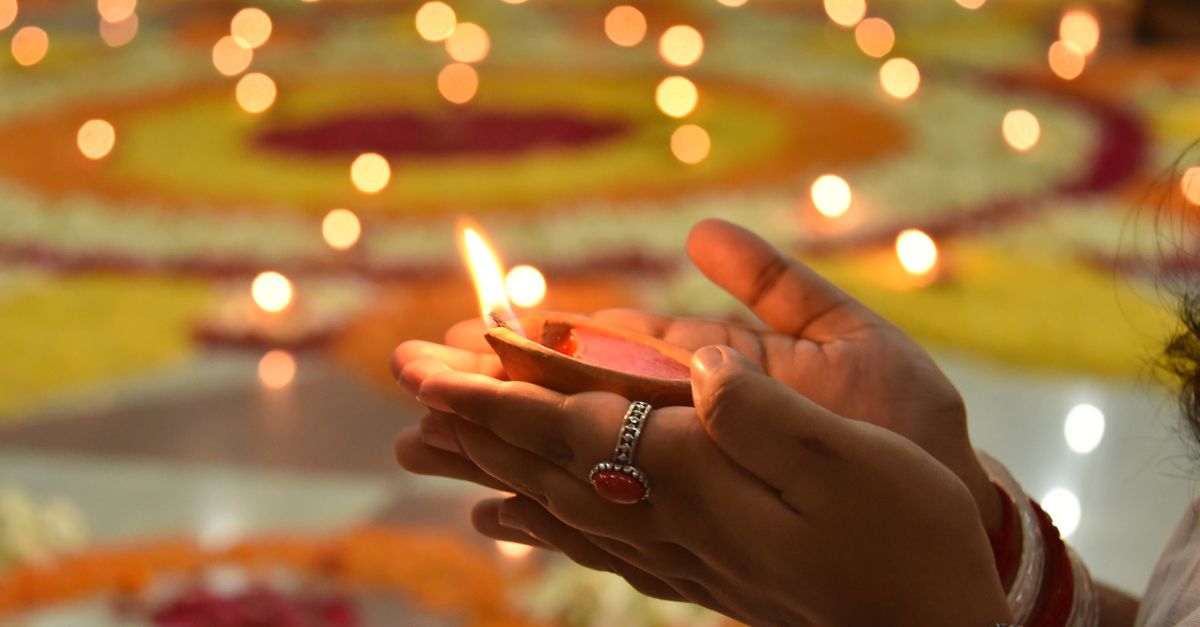 Close-up of a hand holding a lit candle during a religious ceremony surrounded by glowing lights.