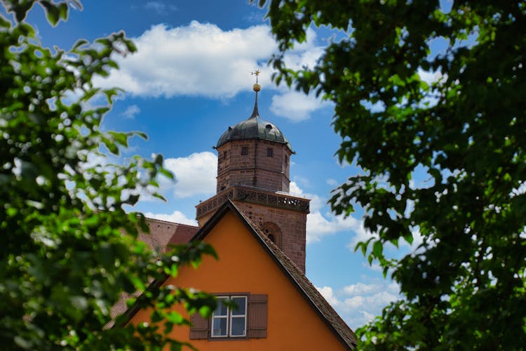 A Church Tower Behind A House On The Background Of Blue Sky